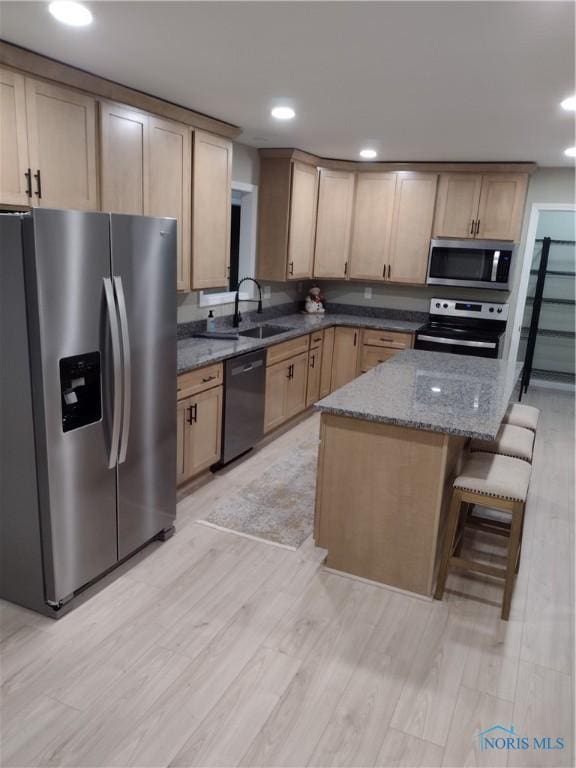 kitchen featuring appliances with stainless steel finishes, light brown cabinetry, sink, dark stone countertops, and a breakfast bar area