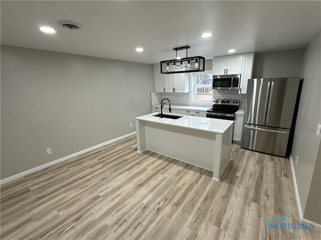 kitchen with white cabinetry, sink, stainless steel appliances, an island with sink, and light wood-type flooring