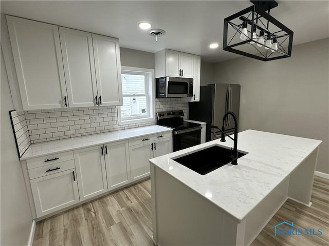 kitchen featuring light stone countertops, appliances with stainless steel finishes, sink, a center island with sink, and white cabinetry