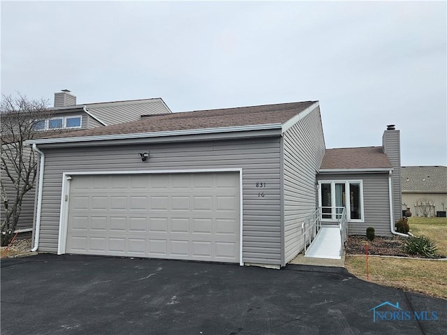 view of front facade with aphalt driveway, a chimney, an attached garage, and a shingled roof