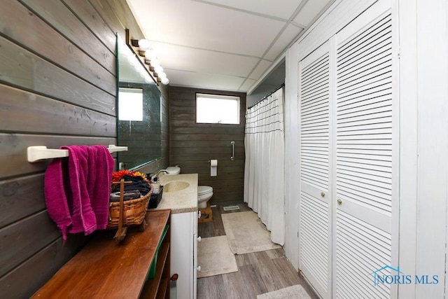 bathroom featuring vanity, toilet, wood-type flooring, and wooden walls