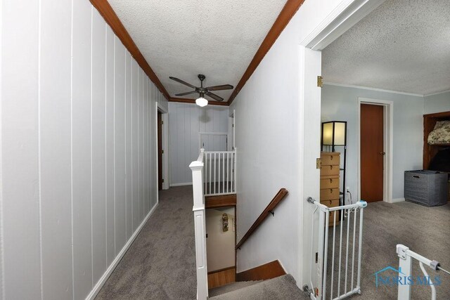 corridor with wooden walls, a textured ceiling, carpet floors, and ornamental molding