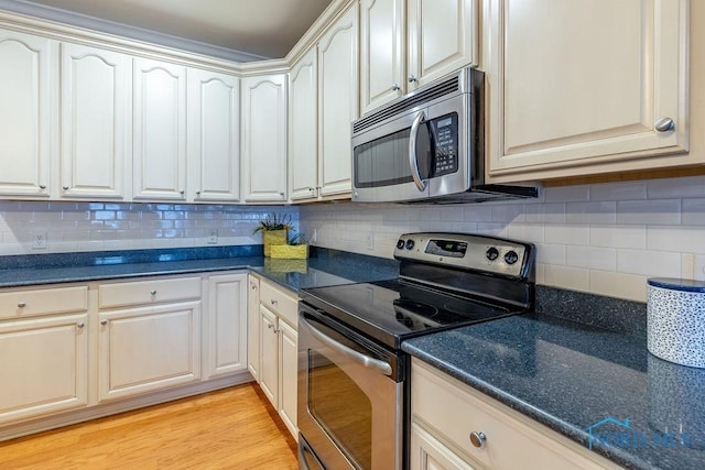 kitchen with tasteful backsplash, light hardwood / wood-style floors, dark stone counters, and appliances with stainless steel finishes