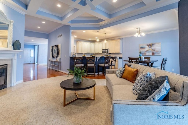 living room with coffered ceiling, ornamental molding, a tile fireplace, beam ceiling, and light hardwood / wood-style floors