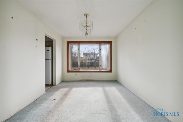 spare room featuring light carpet and a chandelier