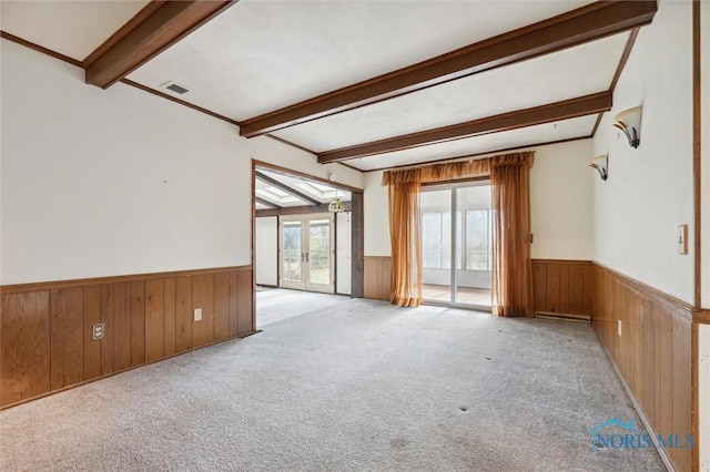 unfurnished room with beamed ceiling, wood walls, light carpet, and french doors