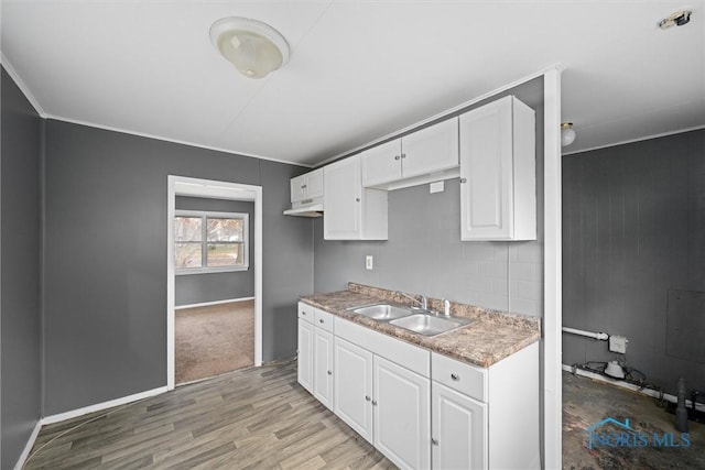 kitchen with white cabinets, light wood-type flooring, sink, and wooden walls