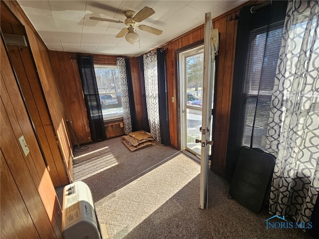 doorway to outside featuring wooden walls, carpet floors, and ceiling fan