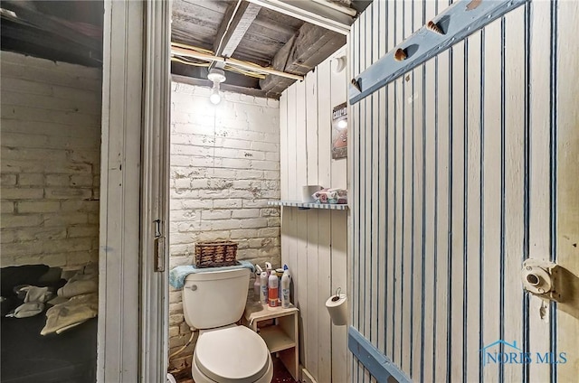 bathroom featuring brick wall and toilet