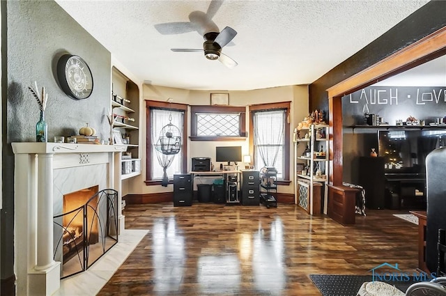 home office featuring built in shelves, a textured ceiling, ceiling fan, a tile fireplace, and wood-type flooring