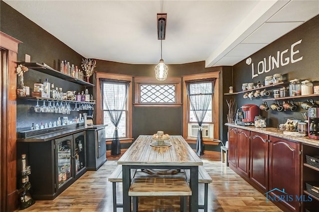 bar with decorative light fixtures, cooling unit, and light wood-type flooring