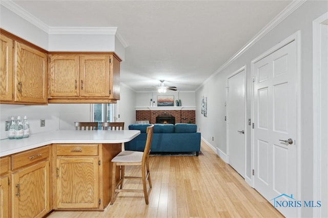 kitchen featuring kitchen peninsula, a kitchen bar, ceiling fan, crown molding, and light hardwood / wood-style flooring