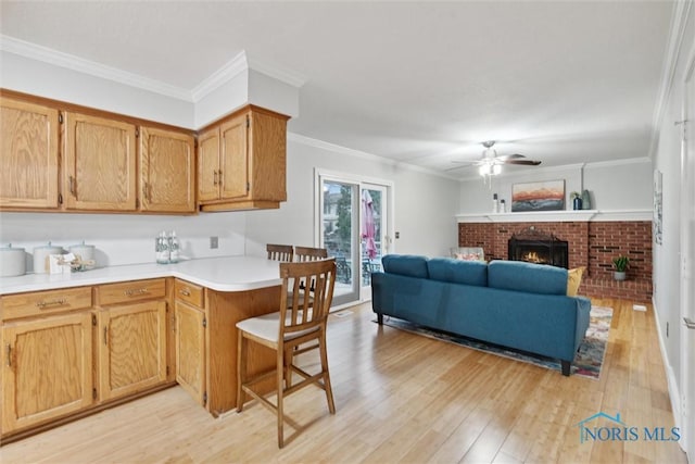 kitchen with ceiling fan, a brick fireplace, a kitchen breakfast bar, light wood-type flooring, and ornamental molding