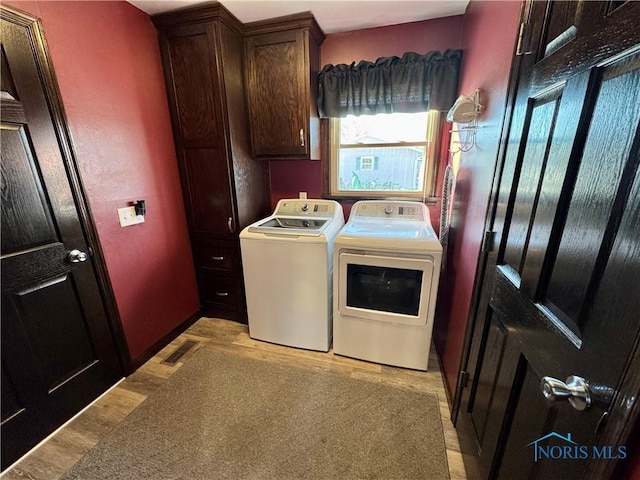 laundry area with cabinets, light hardwood / wood-style flooring, and washing machine and clothes dryer