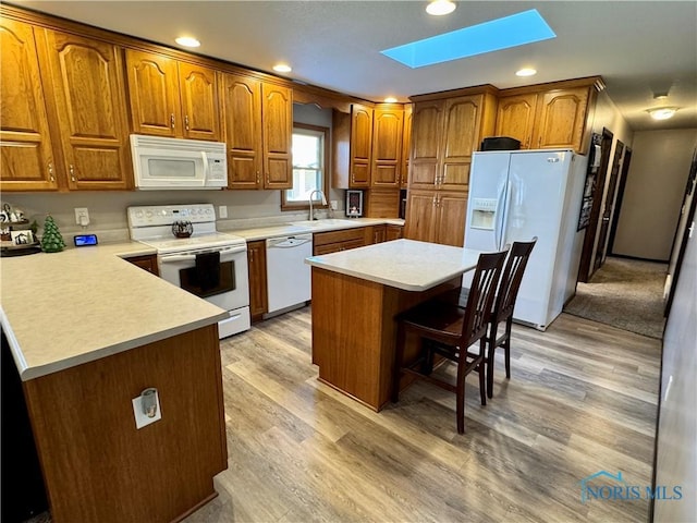 kitchen featuring white appliances, sink, light hardwood / wood-style flooring, a skylight, and a kitchen island