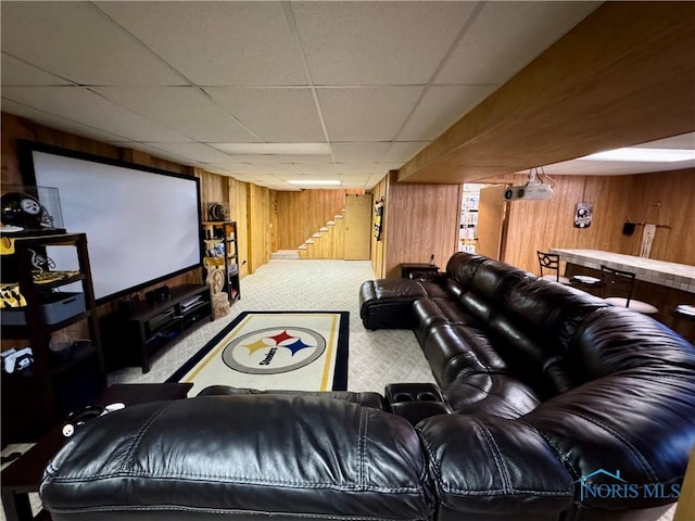 carpeted home theater featuring a paneled ceiling and wooden walls