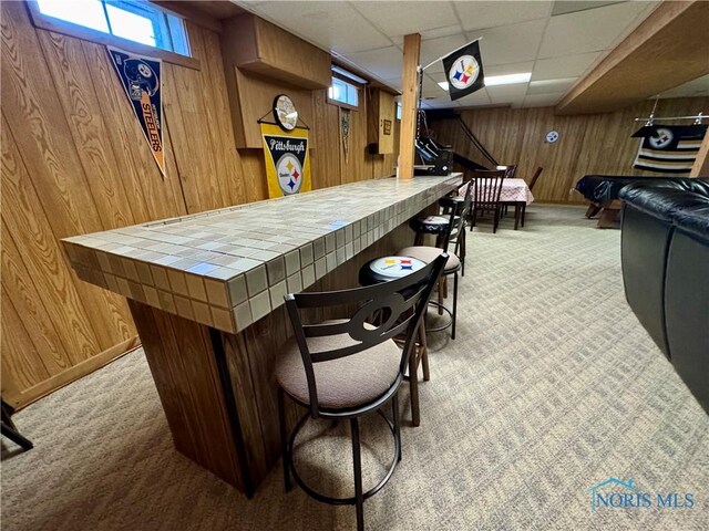 bar featuring a paneled ceiling, tile countertops, plenty of natural light, and wooden walls