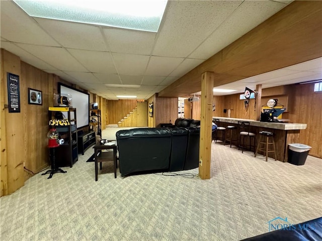 game room featuring a drop ceiling, carpet floors, wooden walls, and bar area