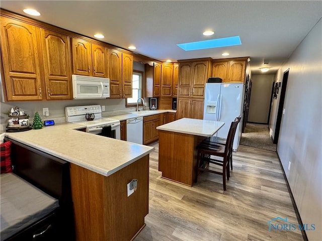 kitchen with a center island, white appliances, light hardwood / wood-style flooring, a skylight, and a breakfast bar area