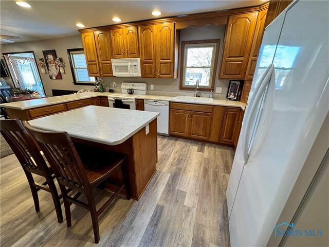 kitchen with sink, kitchen peninsula, light hardwood / wood-style floors, white appliances, and a breakfast bar area