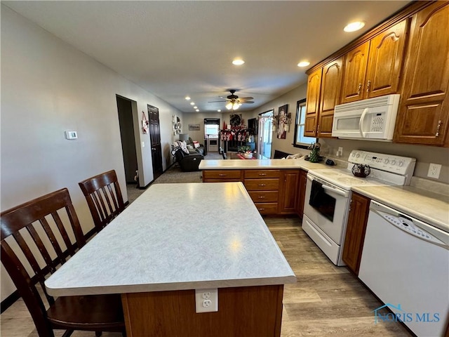 kitchen featuring light hardwood / wood-style flooring, a kitchen breakfast bar, white appliances, ceiling fan, and kitchen peninsula