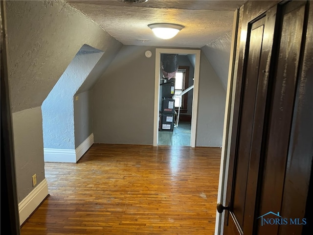 additional living space featuring hardwood / wood-style floors, a textured ceiling, and vaulted ceiling