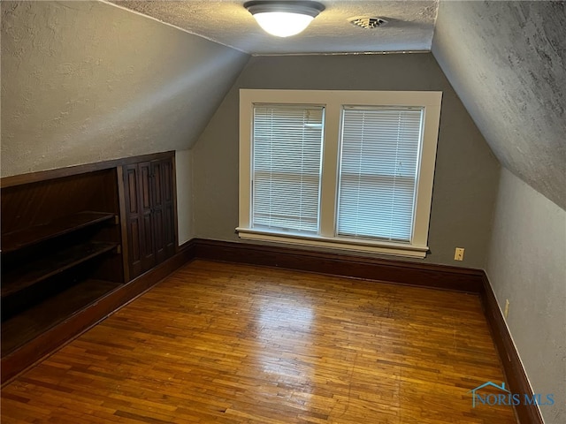 bonus room featuring plenty of natural light, wood-type flooring, a textured ceiling, and vaulted ceiling