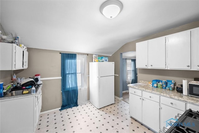 kitchen featuring lofted ceiling, white refrigerator, plenty of natural light, and white cabinetry