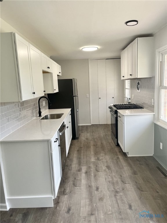 kitchen featuring decorative backsplash, stainless steel appliances, sink, wood-type flooring, and white cabinets