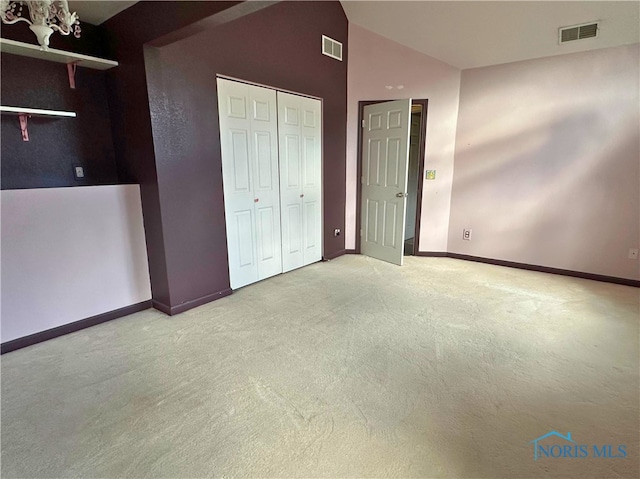 unfurnished bedroom with light carpet, high vaulted ceiling, an inviting chandelier, and a closet