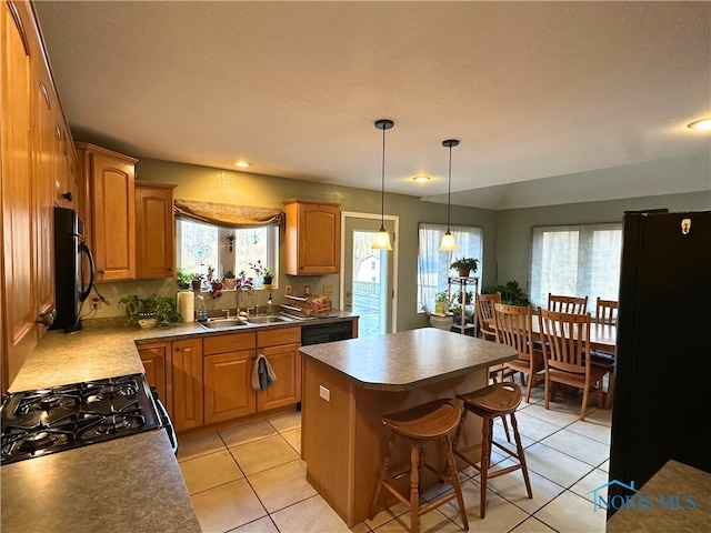 kitchen featuring a center island, sink, a breakfast bar area, light tile patterned flooring, and black appliances