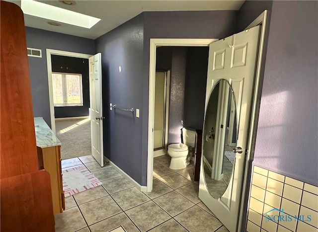 bathroom with tile patterned flooring, toilet, and a skylight