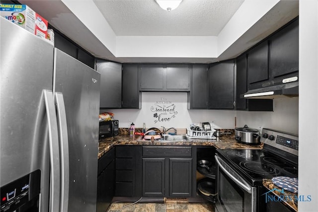 kitchen with sink, dark stone countertops, a textured ceiling, appliances with stainless steel finishes, and a tray ceiling