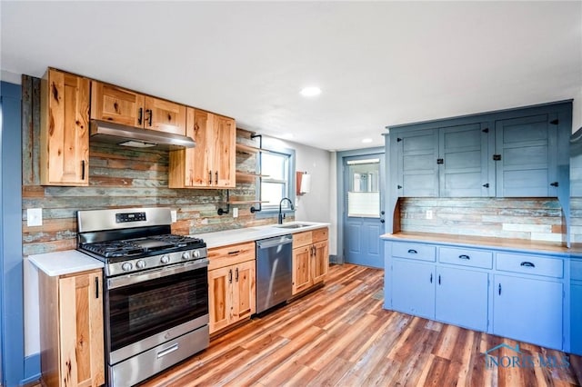 kitchen featuring sink, light wood-type flooring, blue cabinetry, appliances with stainless steel finishes, and tasteful backsplash