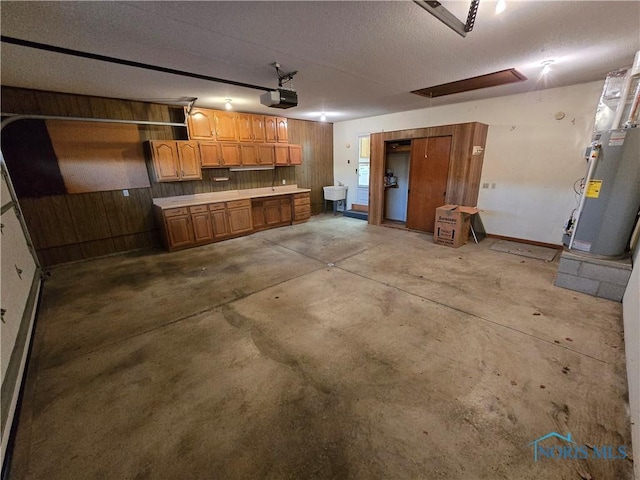 garage featuring wood walls, sink, water heater, and a garage door opener