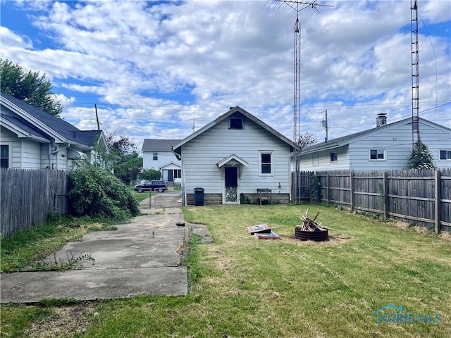 back of house with a fire pit and a lawn