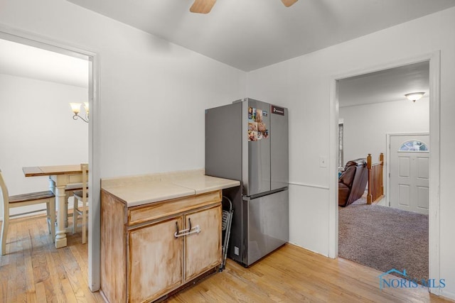 kitchen with stainless steel fridge, ceiling fan with notable chandelier, and light hardwood / wood-style flooring