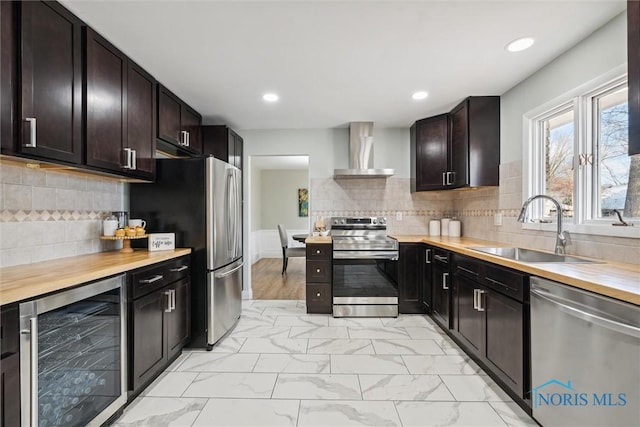 kitchen featuring butcher block counters, sink, wall chimney exhaust hood, stainless steel appliances, and wine cooler