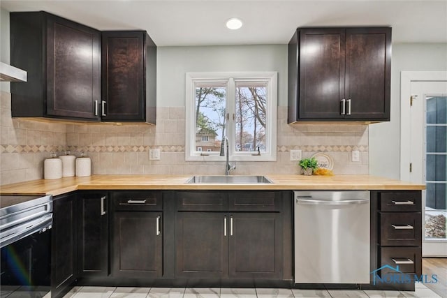 kitchen featuring dark brown cabinetry, sink, wall chimney exhaust hood, wooden counters, and appliances with stainless steel finishes