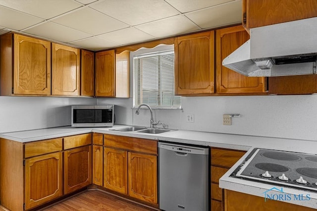 kitchen with a paneled ceiling, stainless steel appliances, extractor fan, sink, and light hardwood / wood-style floors