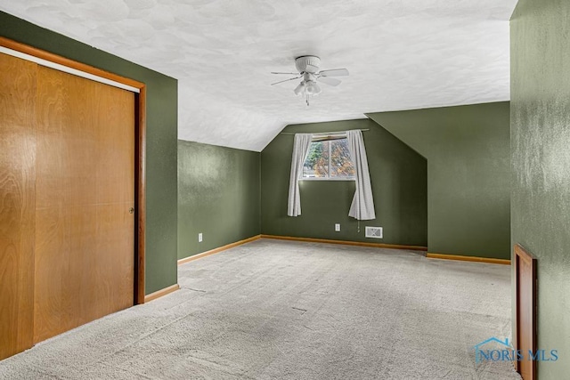 additional living space with carpet flooring, a textured ceiling, vaulted ceiling, and ceiling fan