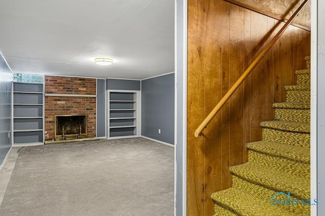 unfurnished living room with built in shelves, carpet floors, a brick fireplace, and wood walls