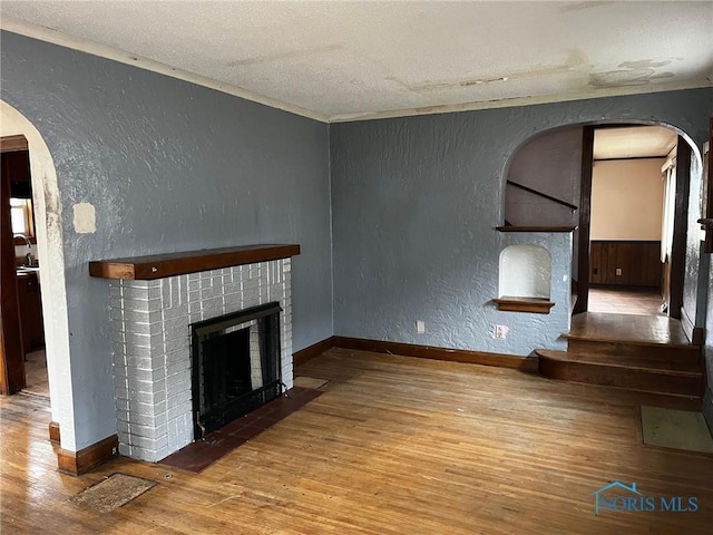 unfurnished living room with hardwood / wood-style flooring, a textured ceiling, and a brick fireplace