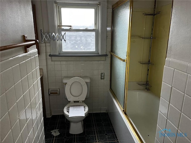 bathroom with tile patterned flooring, toilet, combined bath / shower with glass door, and tile walls