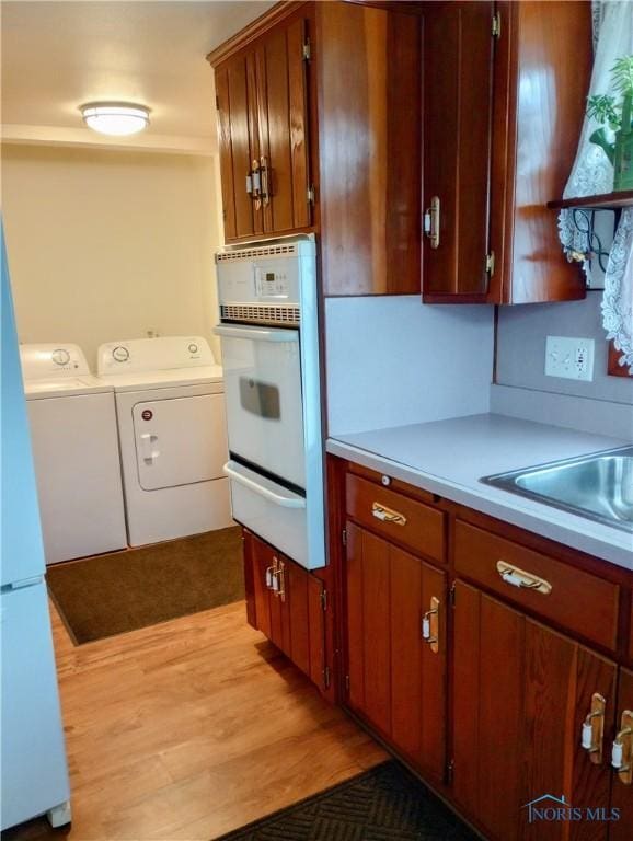 kitchen featuring washer and dryer, light wood-type flooring, oven, and sink