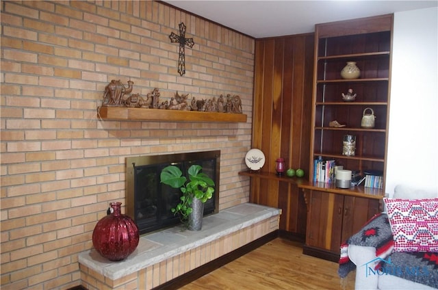 living room with a large fireplace, light hardwood / wood-style floors, and brick wall