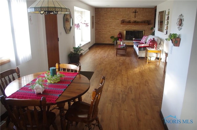 dining space featuring a fireplace, wood-type flooring, and brick wall