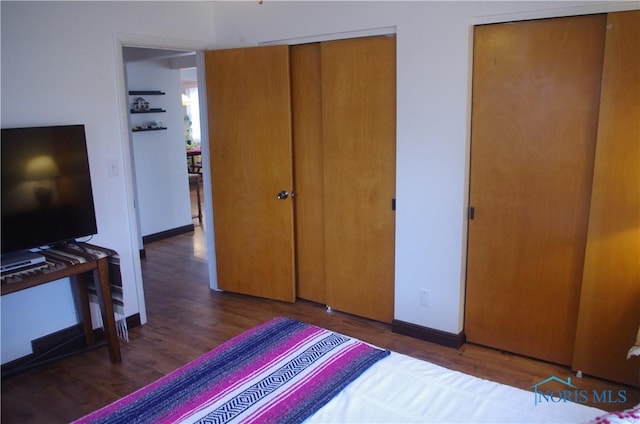 bedroom with dark hardwood / wood-style floors and multiple closets