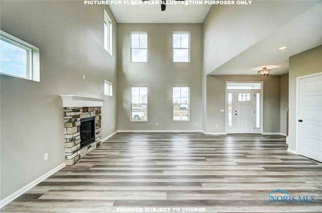 unfurnished living room with a stone fireplace, a towering ceiling, ceiling fan with notable chandelier, and light wood-type flooring