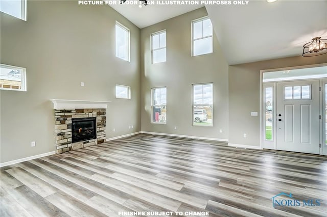 unfurnished living room with a stone fireplace, a towering ceiling, and light wood-type flooring